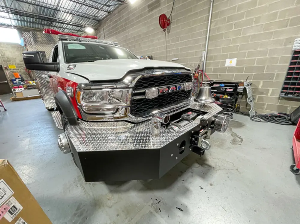 Exterior view of small fire truck showing cab, body compartments, and wheel/tire area.